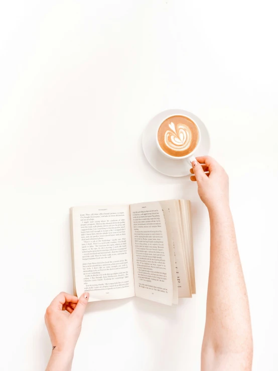 a hand is holding an open book with a cappuccino on top