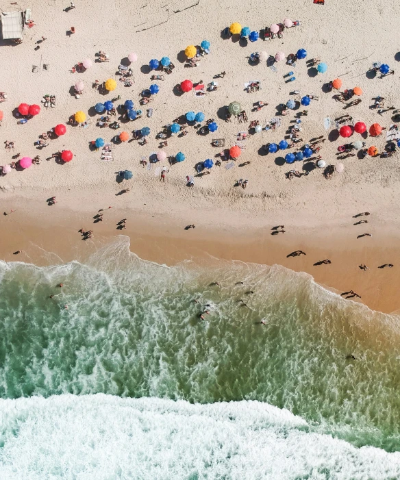 an aerial view of an ocean beach and many people with umbrellas