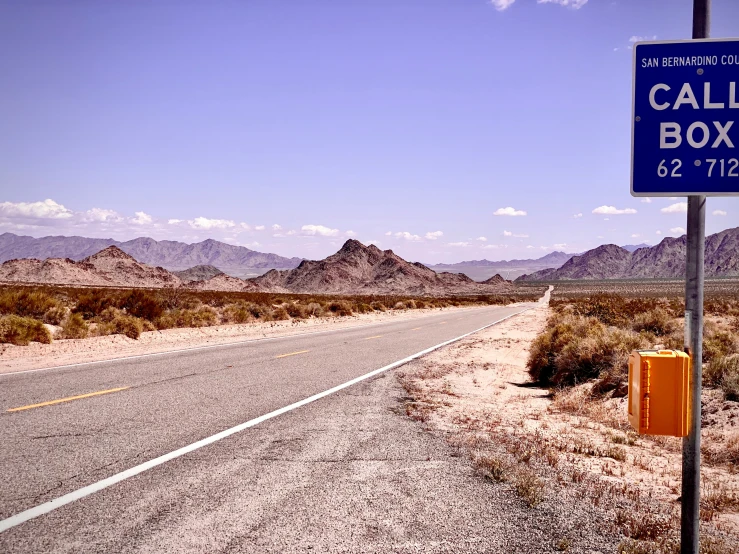 an empty road with mountains in the background and a blue box sign