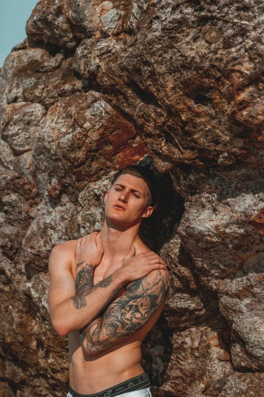 a man wearing  is posed in front of a large rock