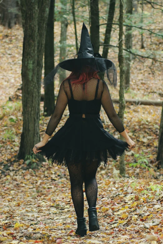 the woman is wearing a witch costume and walking in the woods