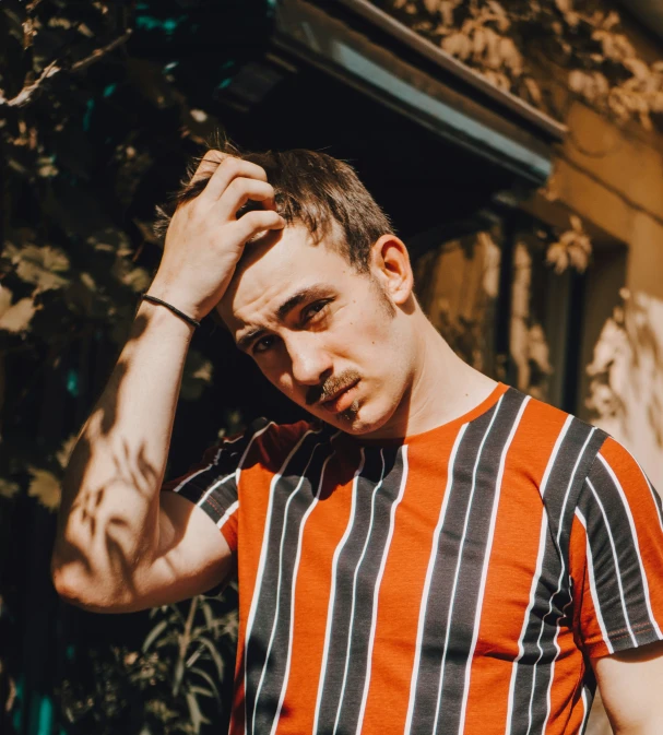 a man with tattoos is standing outside in a striped t - shirt