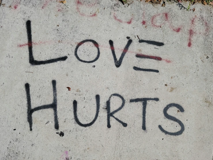 a concrete surface with black writing that says love hurts