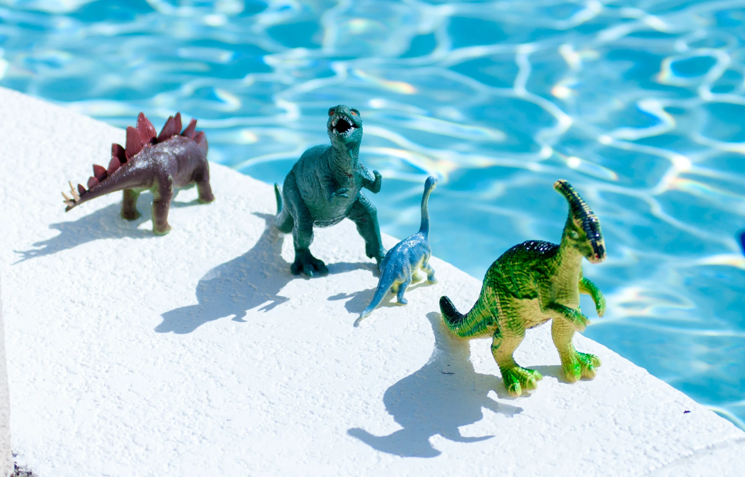 four dinosaur figurines are sitting in front of an icy pool