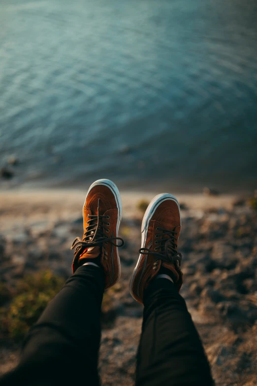 someone wearing shoes stands on a rocky shore by the water