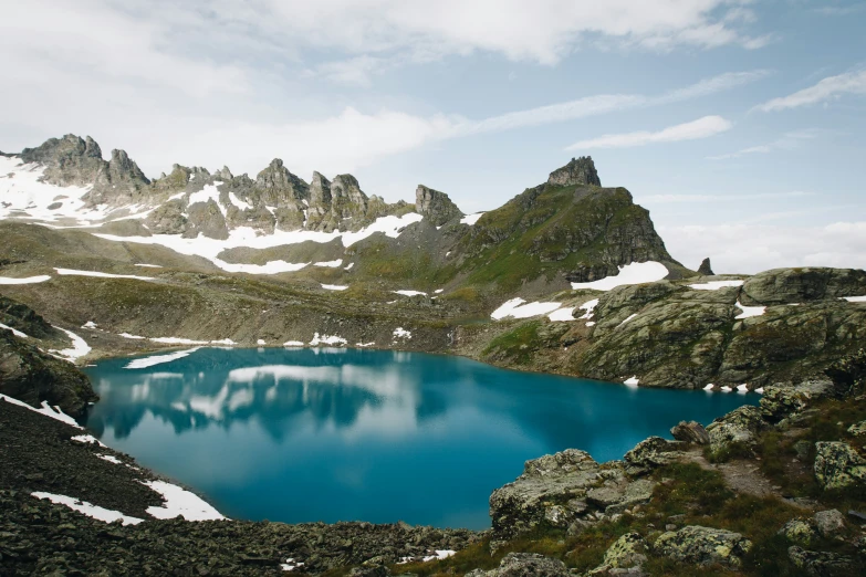 a bright blue pond with some snow on the rocks