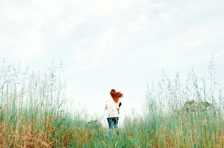 a woman standing alone in tall grass and looking to the sky