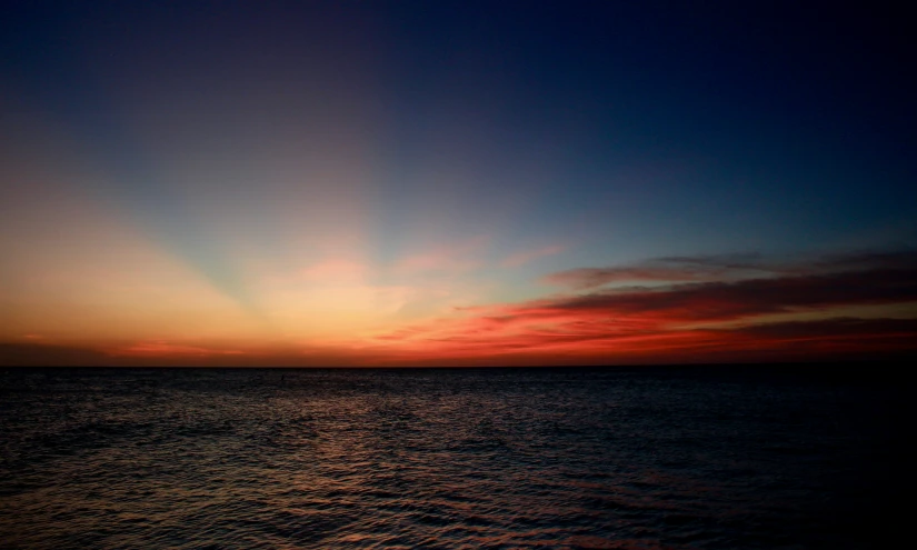 a sunset on the ocean with an airplane in the sky