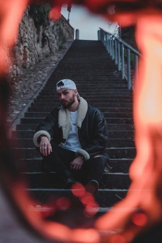 a man sitting on some stairs wearing his hat and scarf