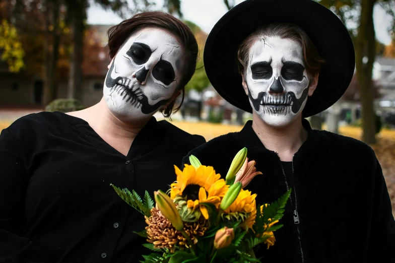 two women with face painted in skeletons holding flowers