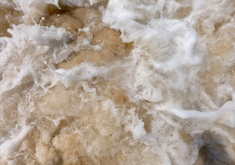 water covered with foam next to a rocky shoreline