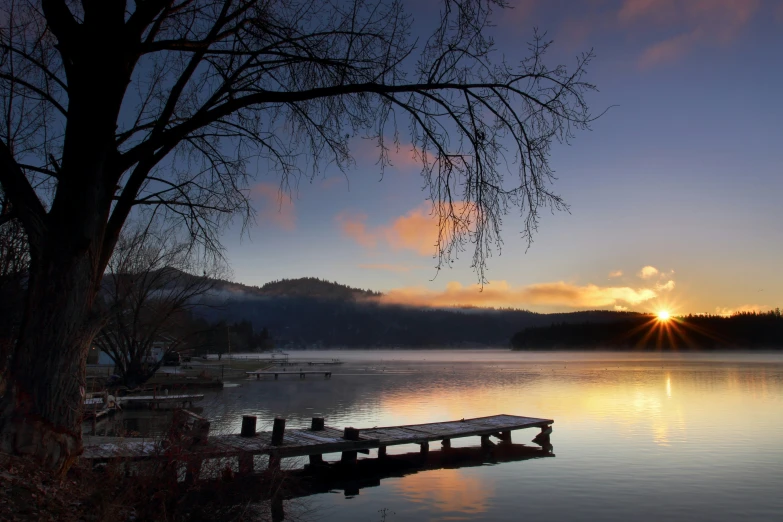 a bench sits on a dock over the water as the sun sets