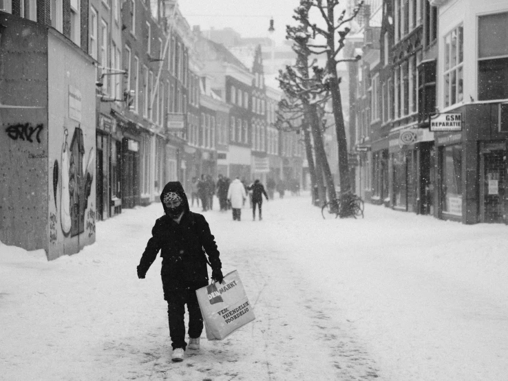 a man walking down a snowy street holding a shopping bag