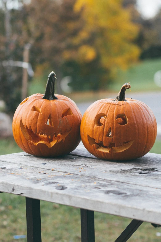 two jack o lanterns sitting on top of a wooden bench