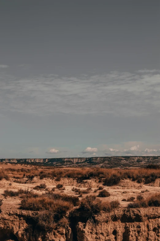 a lone airplane flying over dirt cliffs on an arid plain