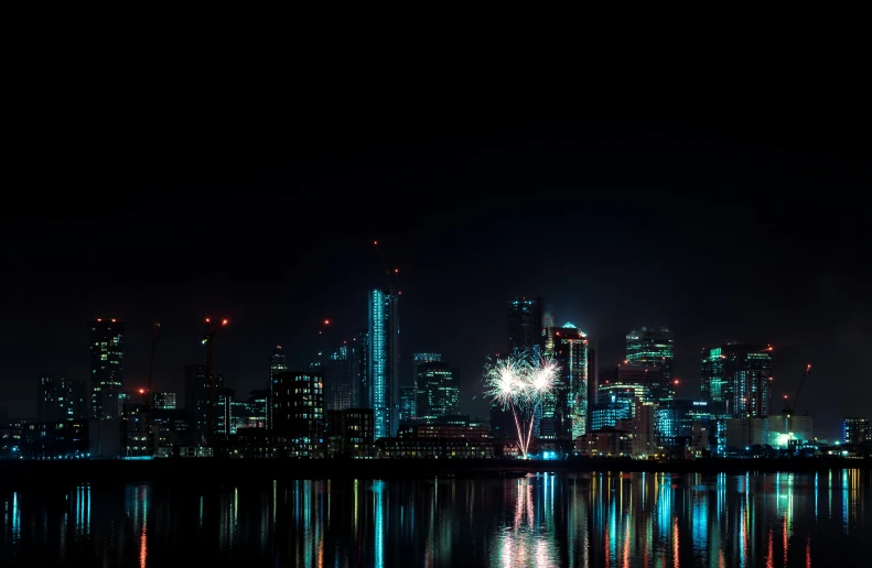 a city view with tall buildings and colorful lights on the water at night