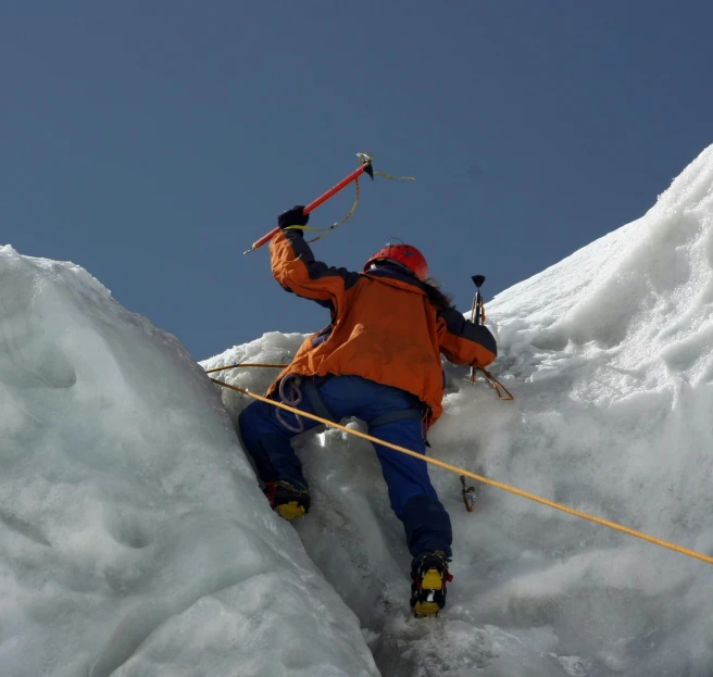 a man in an orange jacket climbing up a snowy mountain