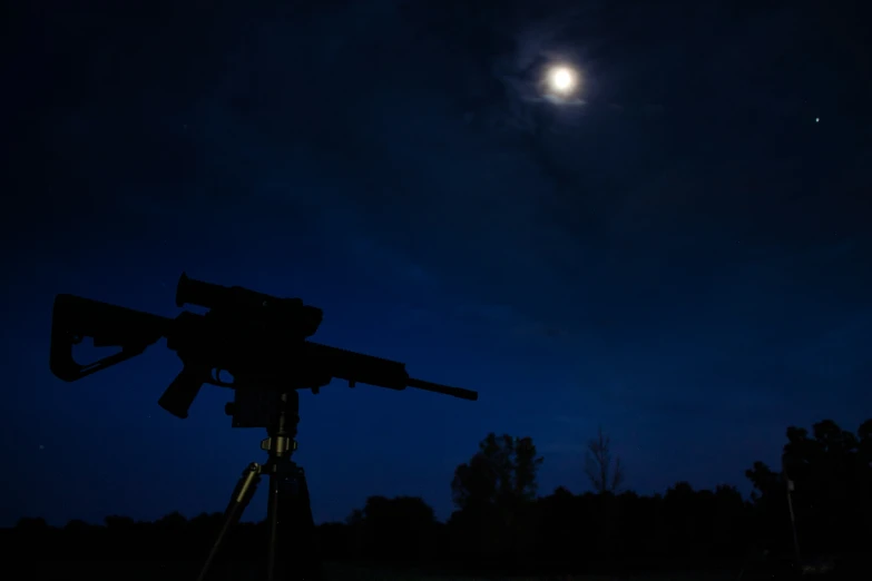 the moon is visible over a rifle on a tripod