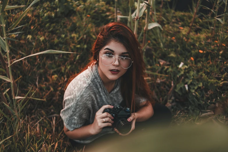 a girl wearing glasses holding a camera in the grass