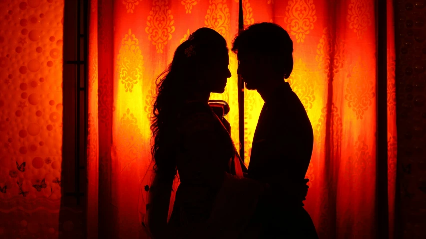 two people standing in silhouette behind red curtain