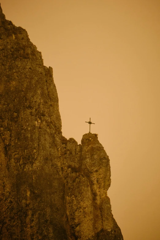 a cross on a rocky cliff, with a foggy sky