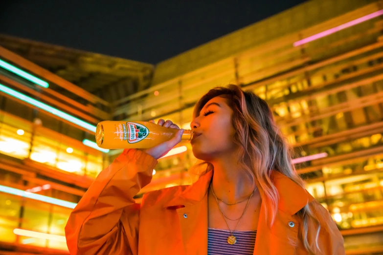 woman with orange jacket and blue shirt drinking from a bottle