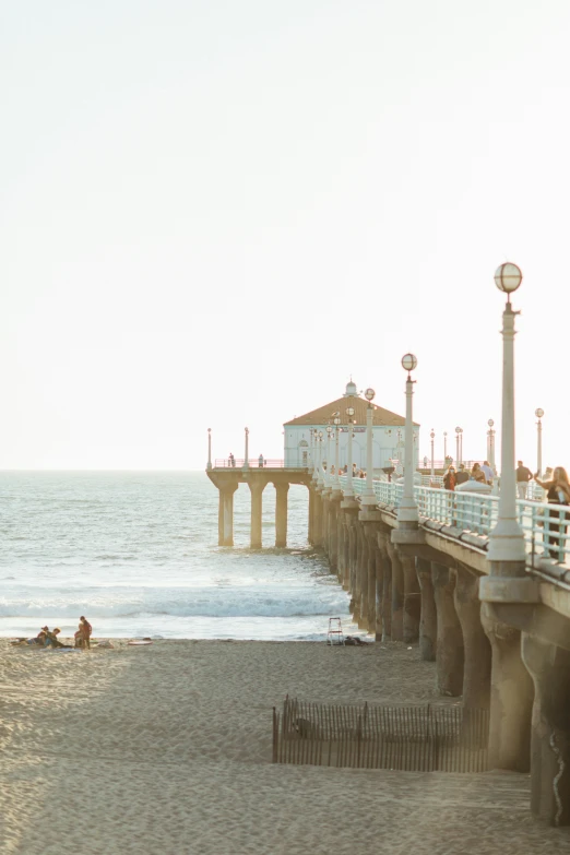 people are standing and laying on the sand at a beach next to a pier