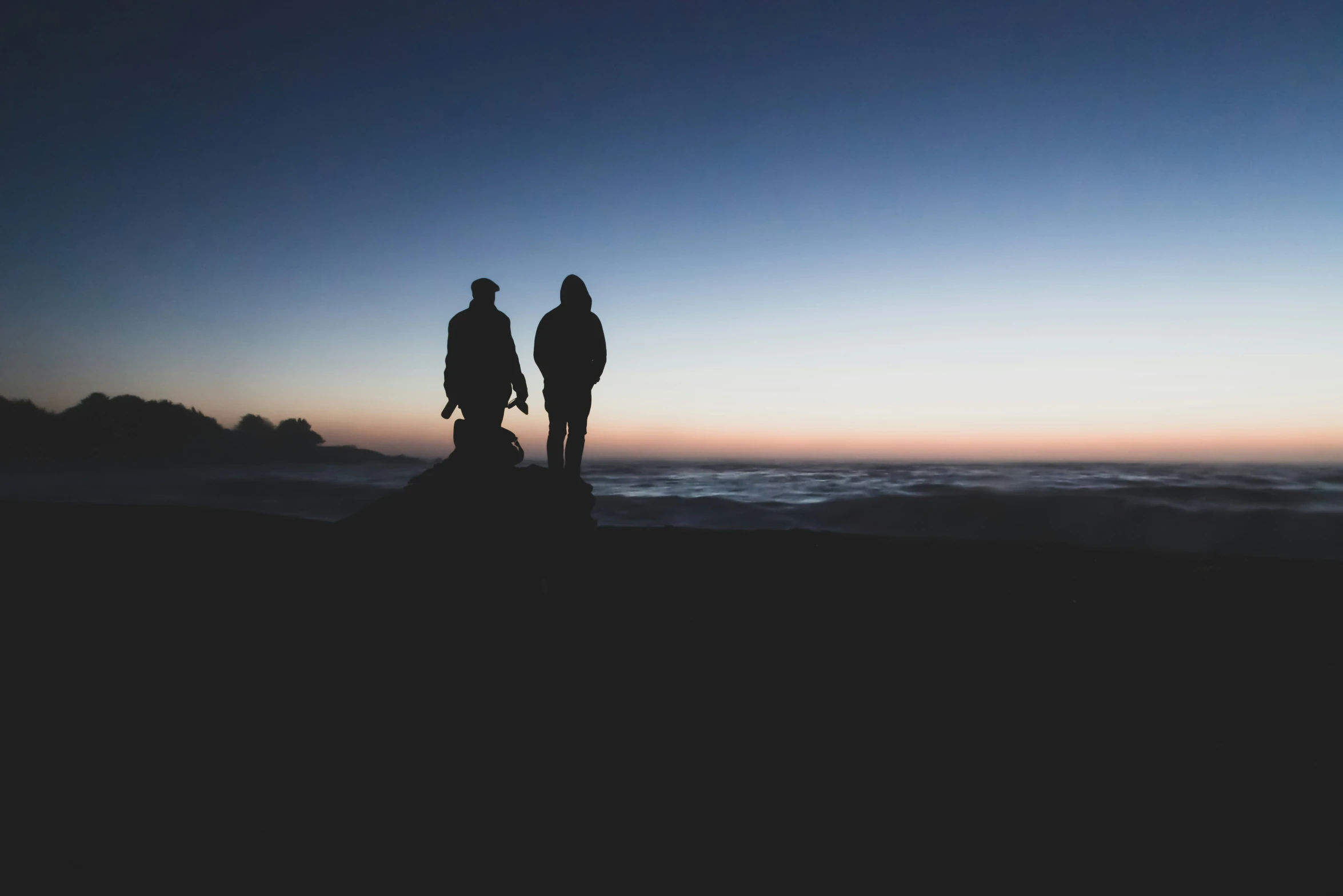 two people standing on a rocky ridge overlooking the ocean