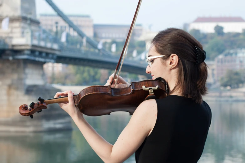 the woman is playing the violin while by the river