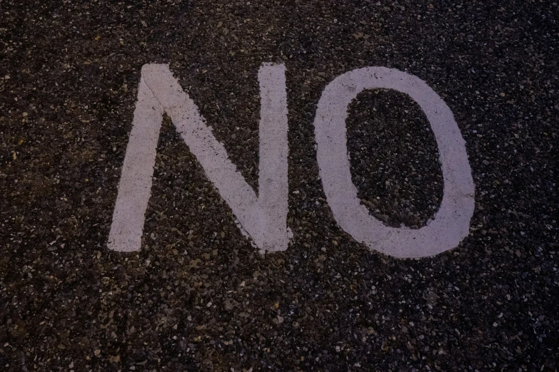 a no parking sign on the asphalt in front of a bus stop