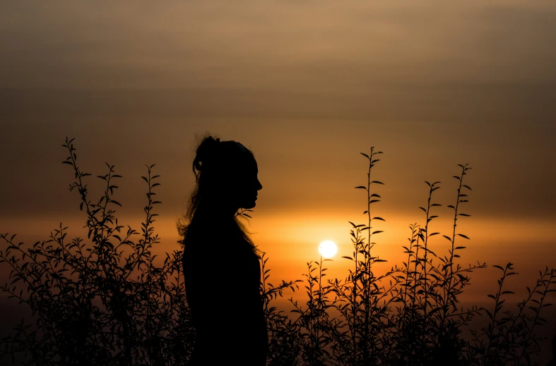 the silhouette of a girl standing in front of the sun