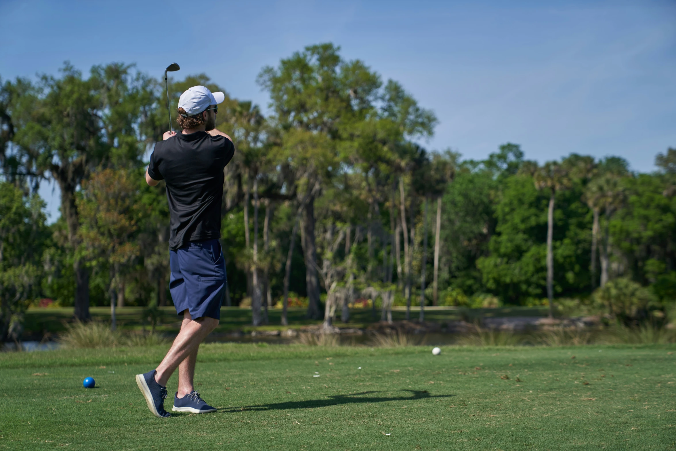 a man in black shirt and blue shorts swinging a golf club