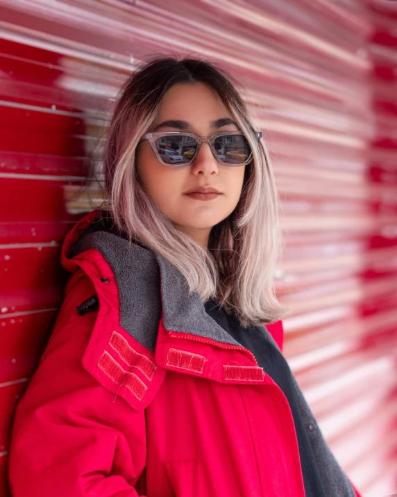 a woman with blonde hair and sunglasses is leaning against a red wall