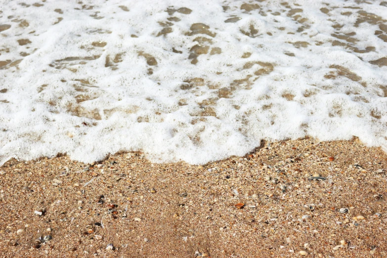 a sandy beach with white foamy water and some brown sand