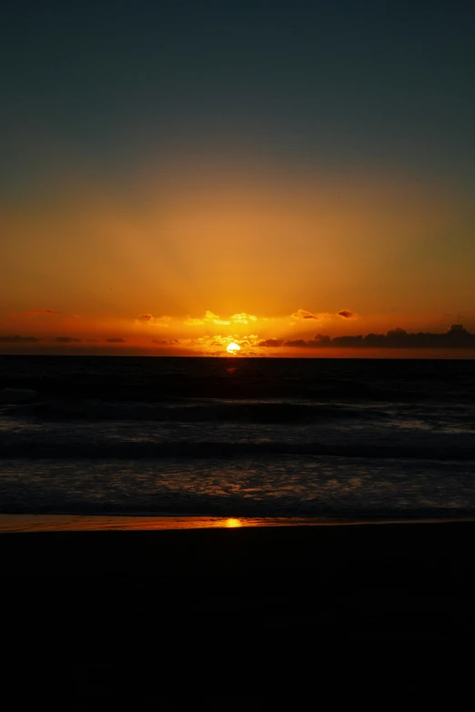 the sun is setting on the ocean, with a surfer riding a board