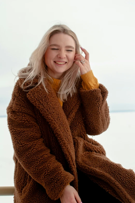 woman in brown coat talking on cellphone at beach