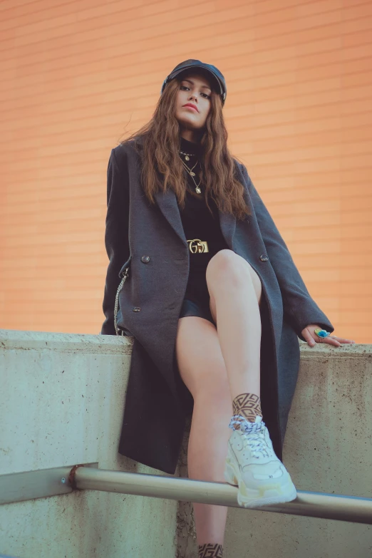 a woman with long hair wearing a hat sits on a wall