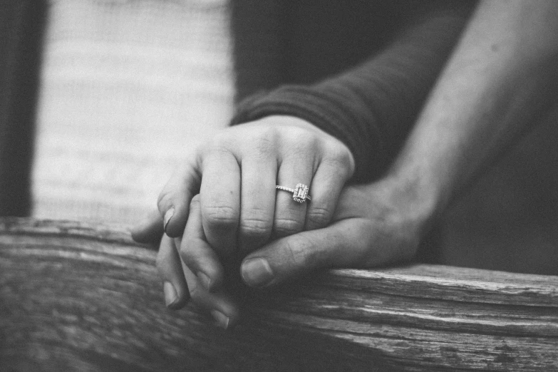 two hands on a wooden table holding the hand of someone else