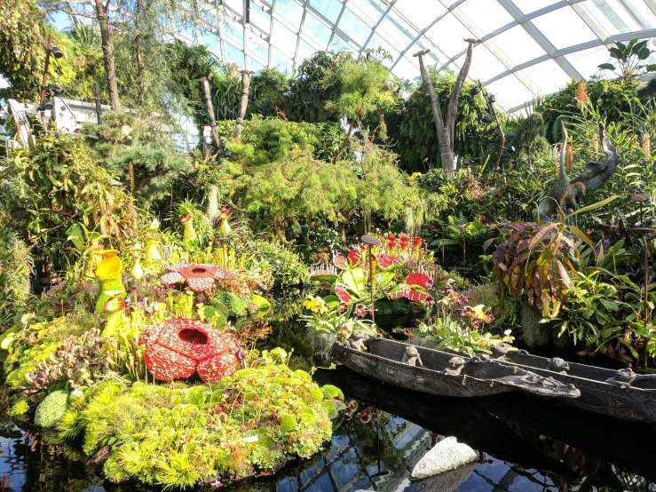 a greenhouse with canoes in a pond filled with flowers