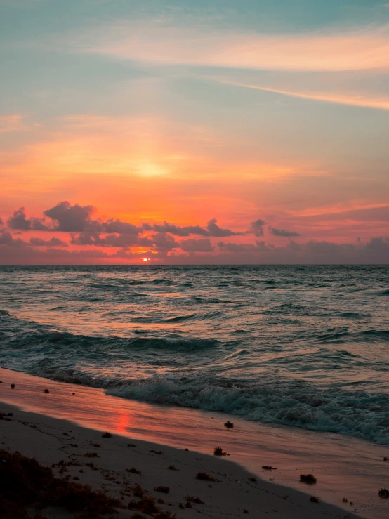 the sun is setting over the water of a beach