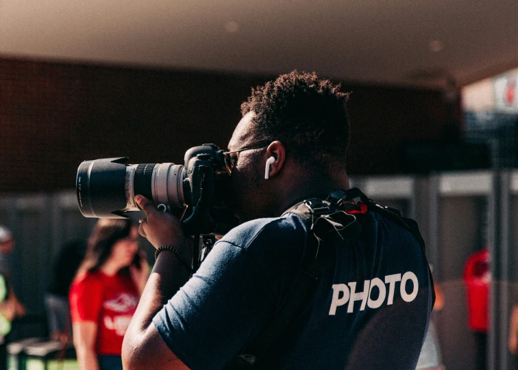 a man with his camera behind him, standing in the shade