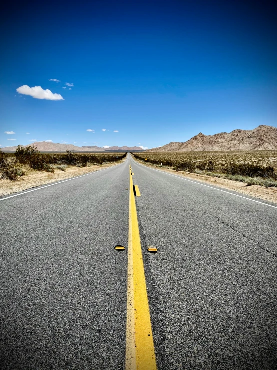 the empty street has long yellow lines and blue sky