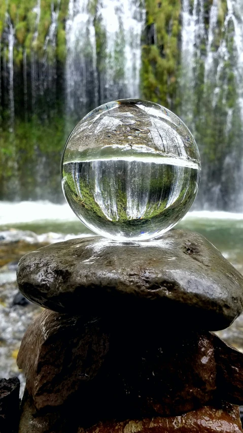 a glass ball sitting on rocks near a waterfall