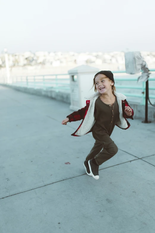 girl runs along pier and smiles while dressed in gray and maroon