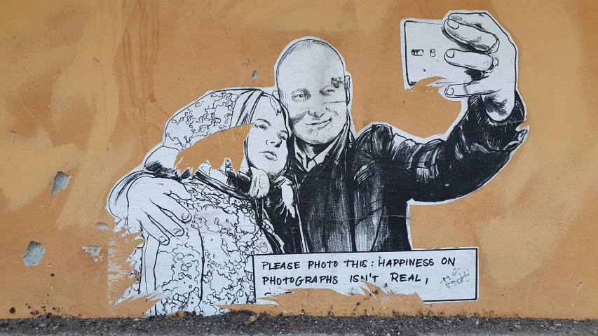 a stencil on the side of a wall with a po of two people pointing at a phone