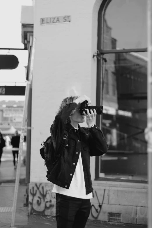 a person with long hair stands on the street with his camera
