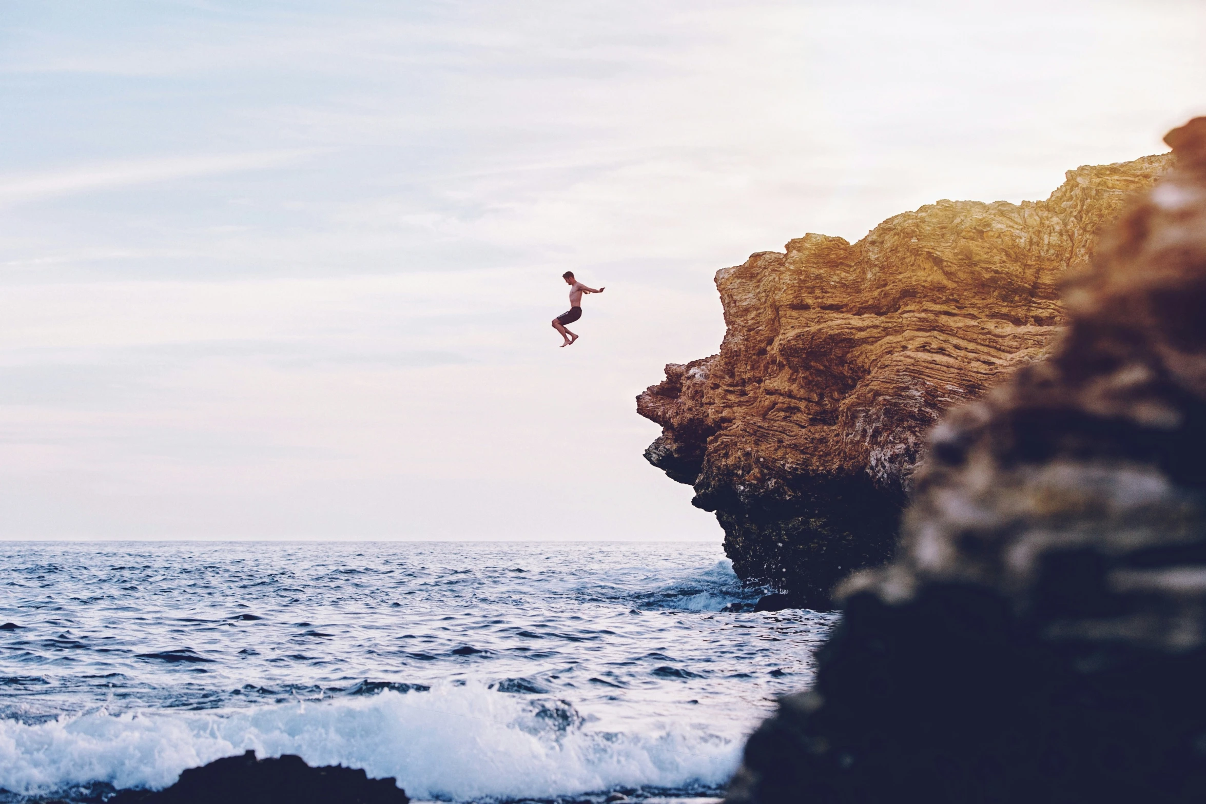 man doing aerial jumping from cliff near ocean