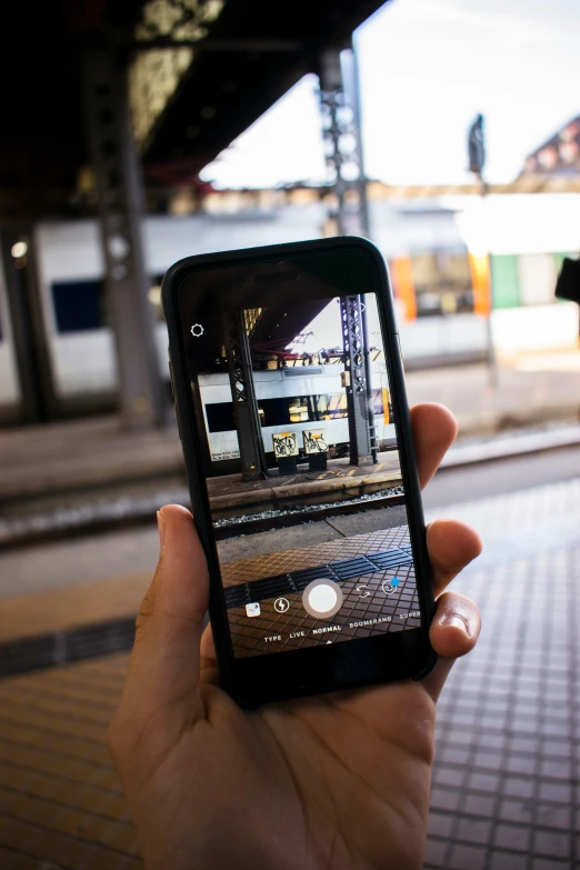 person taking po on smartphone with railway platform in background