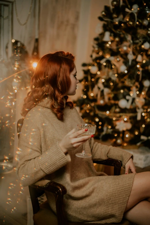 a woman sitting next to a christmas tree in a chair holding a glass