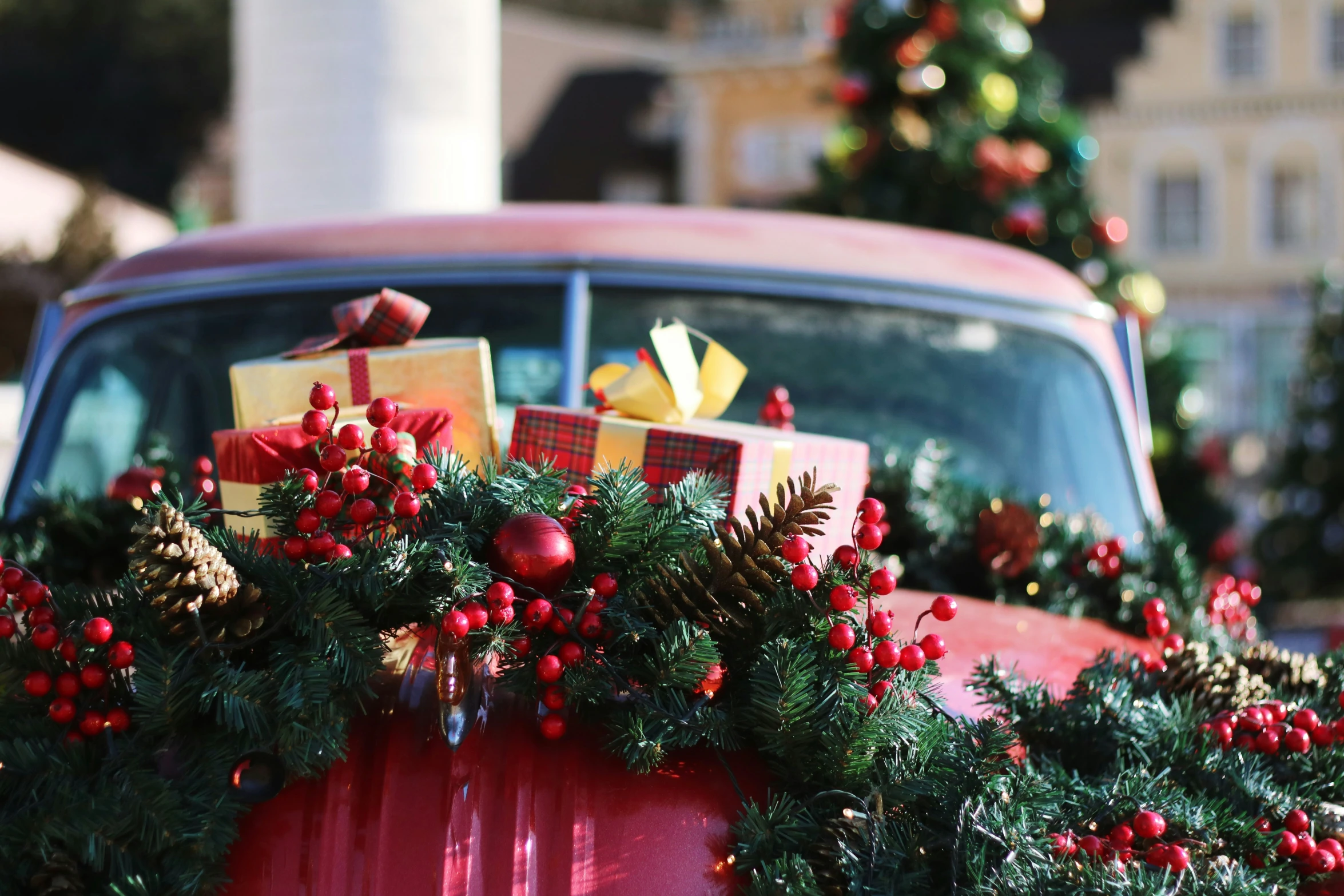 an old truck covered in evergreen, pine cones, and ribbon